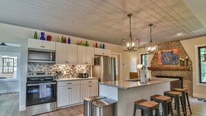 Una cocina moderna con electrodomésticos de acero inoxidable, una isla grande con taburetes de bar y una chimenea de piedra.