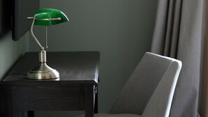 Ein Schreibtisch mit einer grünen Schreibtischlampe, ein Stuhl und ein flachbildschirmfernseher an der Wand.