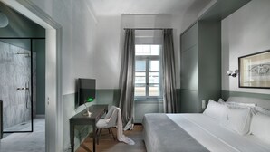 Ein modernes Hotelzimmer mit einem Bett, einem Schreibtisch mit Stuhl, einem Fernseher und einem Fenster mit Vorhängen.
