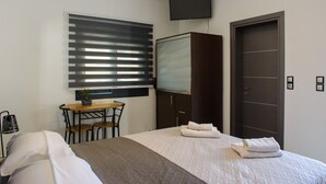 Une chambre d’hôtel avec un lit, un bureau, une chaise, un téléviseur fixé au mur et une porte.