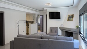 Un salon moderne avec un canapé gris, un téléviseur à écran plat fixé au mur et une cheminée.