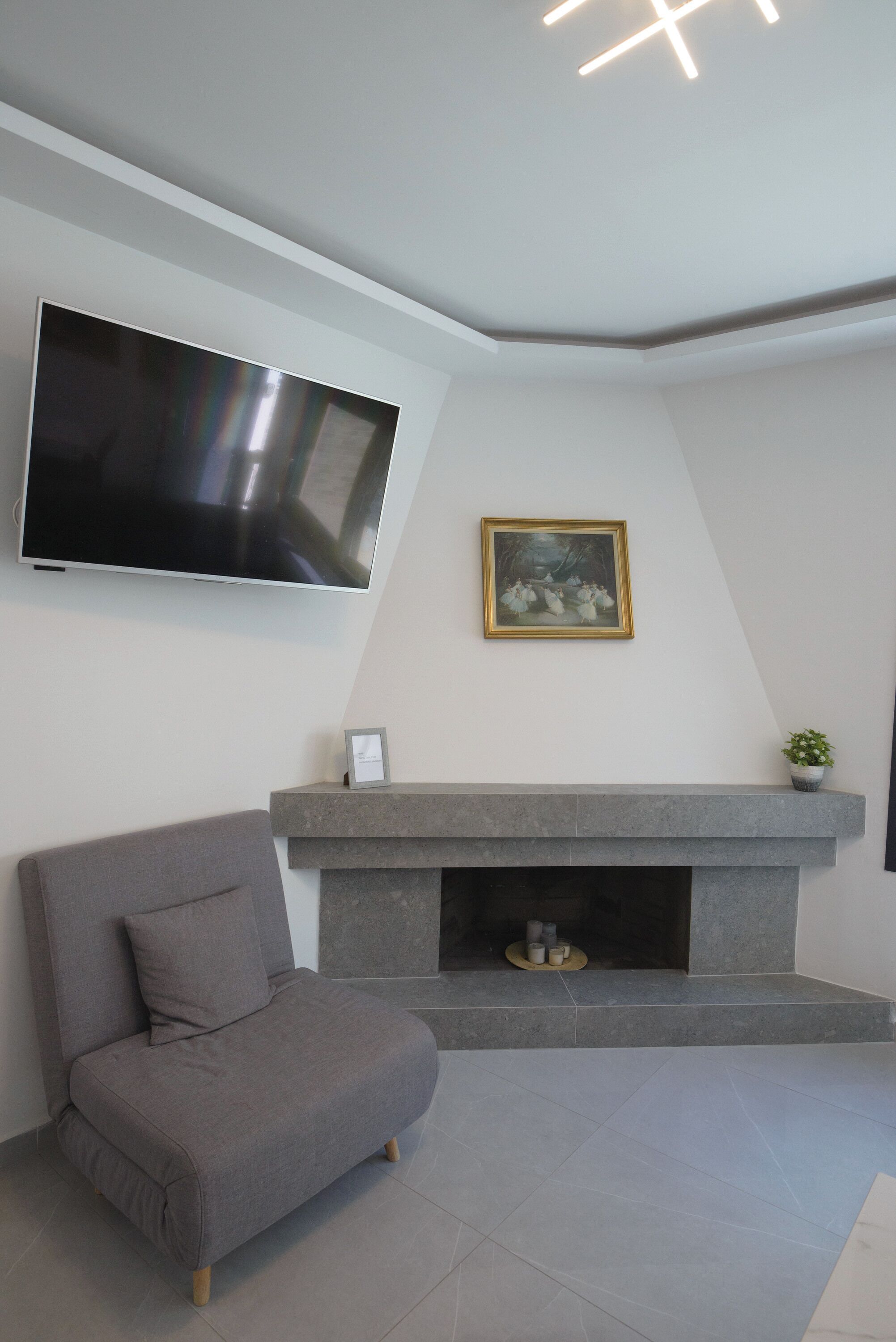 A modern living room with a flat-screen TV, a grey sofa, a fireplace, and a framed picture on the wall.