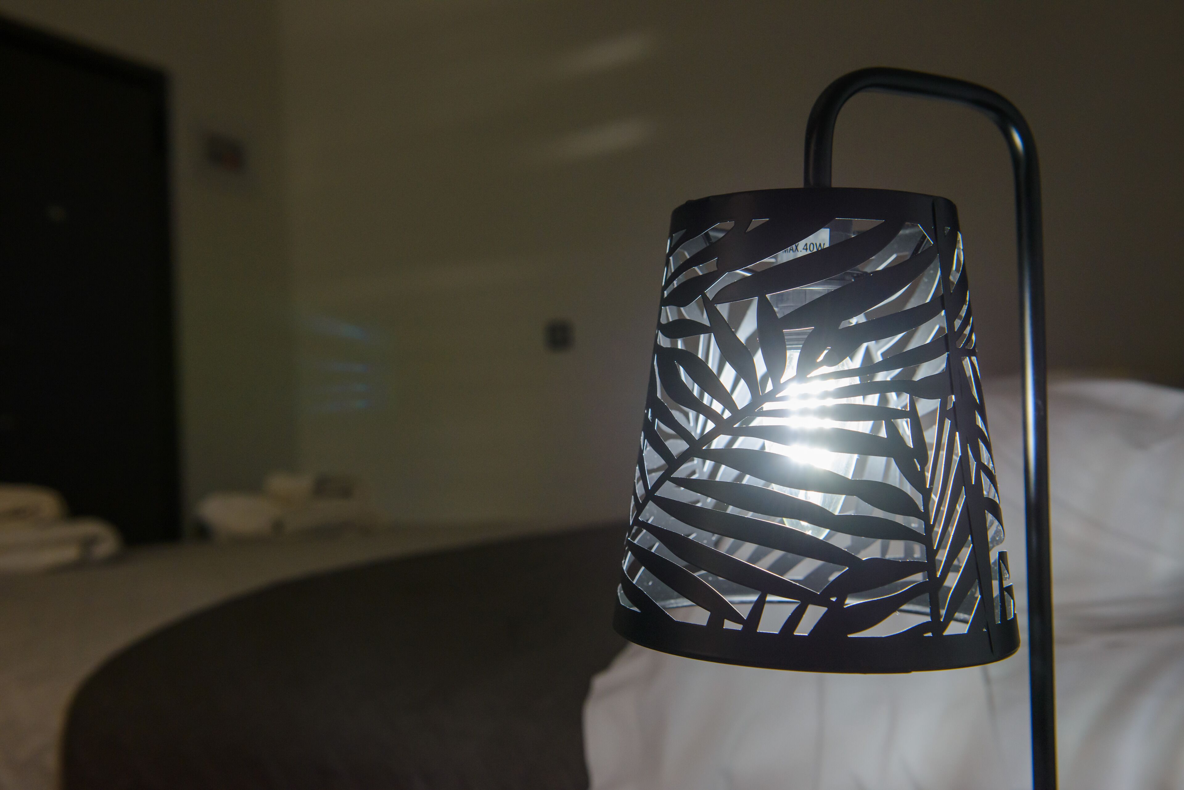 Een close-up van een zwarte metalen lamp met een bladpatroon, geplaatst op een bed in een hotelkamer.