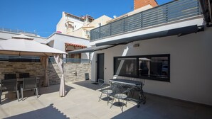 Une terrasse extérieure avec une table et des chaises, un espace salon couvert et une vue sur les bâtiments environnants.