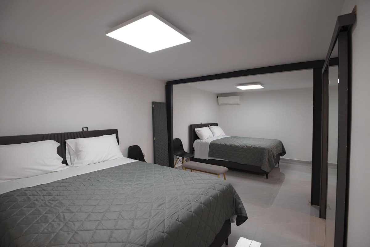 Une chambre d’hôtel moderne avec deux lits, un banc, une chaise et un grand miroir.
