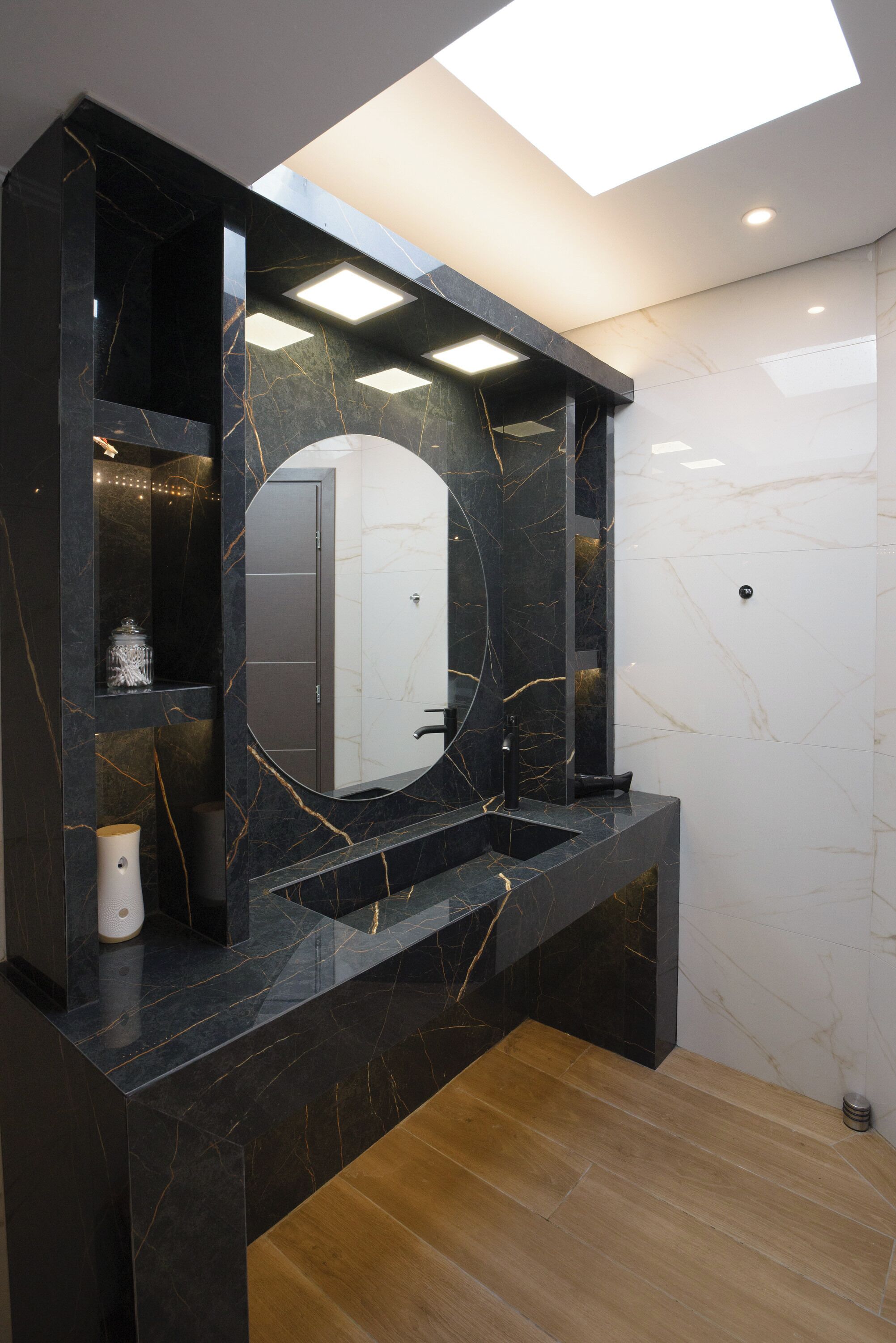 A modern bathroom with a black marble vanity, a large mirror, and a skylight.