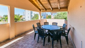 A covered outdoor area with a round table and chairs, a tiled floor, and a view of buildings and trees.