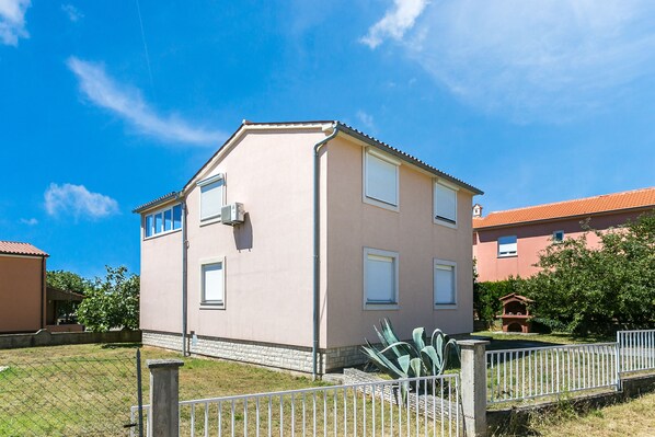 A two-story house with a sloped roof, a small attached garage, and a fenced yard. - Ferienwohnung Kemperle /medulin Kroatien (Medulin)