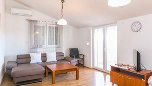 A living room with a sofa, a coffee table, a TV on a wooden cabinet, and a window with curtains.