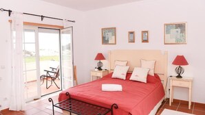 Un dormitorio con cama, dos mesitas de noche con lámparas, una ventana con cortinas y vistas al exterior.