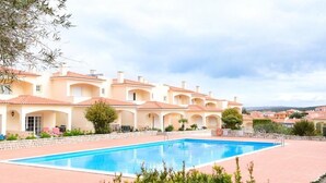 Una piscina rodeada por una hilera de villas de estilo mediterráneo con puertas arqueadas y techos de tejas.