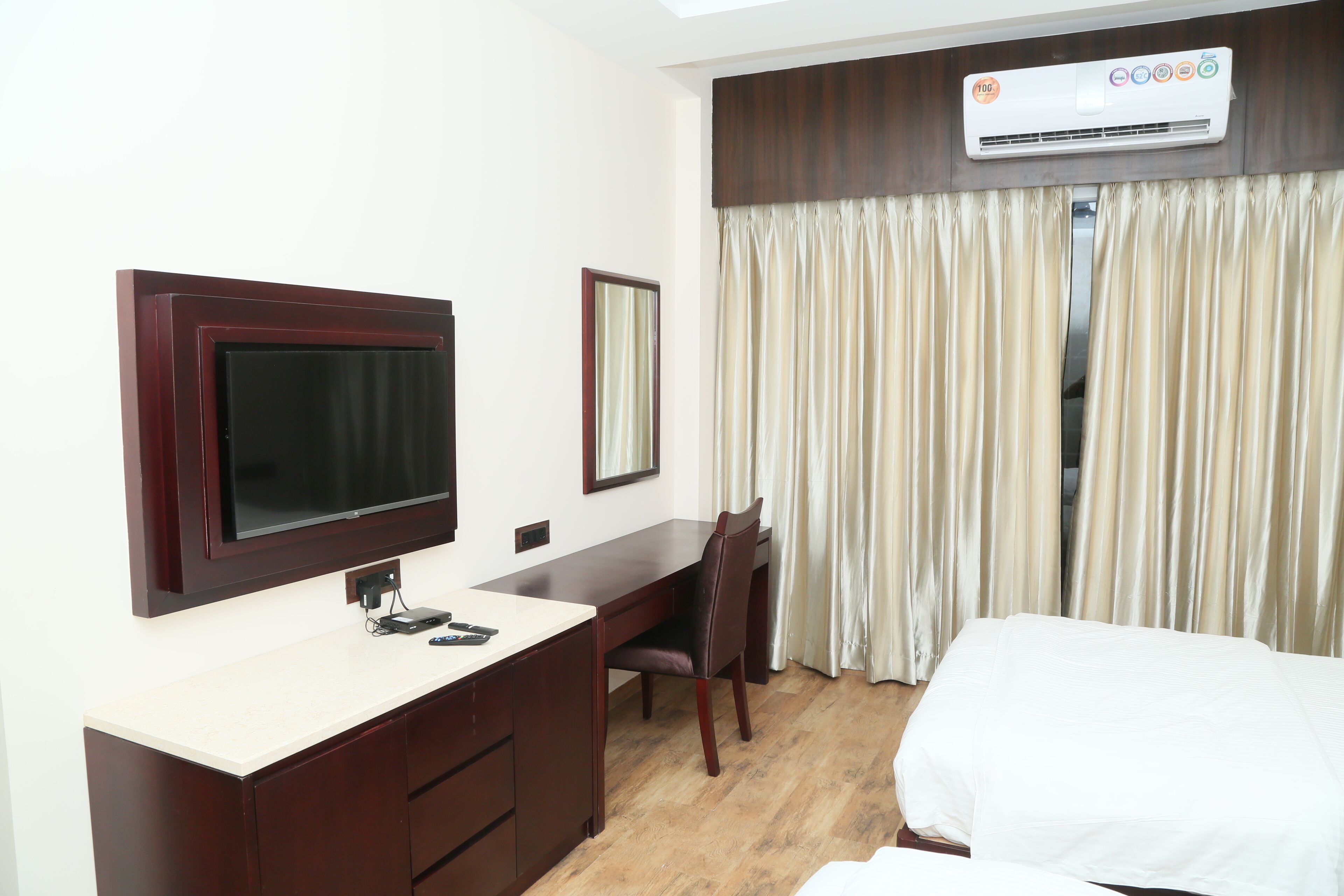 Une chambre d’hôtel comprenant un lit, un bureau avec une chaise, un téléviseur fixé au mur et un appareil de climatisation placé au-dessus des rideaux.