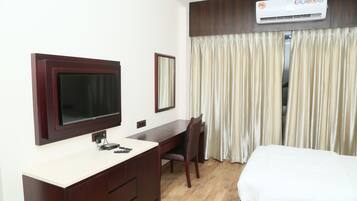 Une chambre d’hôtel comprenant un lit, un bureau avec une chaise, un téléviseur fixé au mur et un appareil de climatisation placé au-dessus des rideaux.