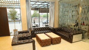 A modern lobby with a sectional sofa and ottomans, a glass partition, and a view of the street. - Hotel Ruturaj Regency (Dhule)