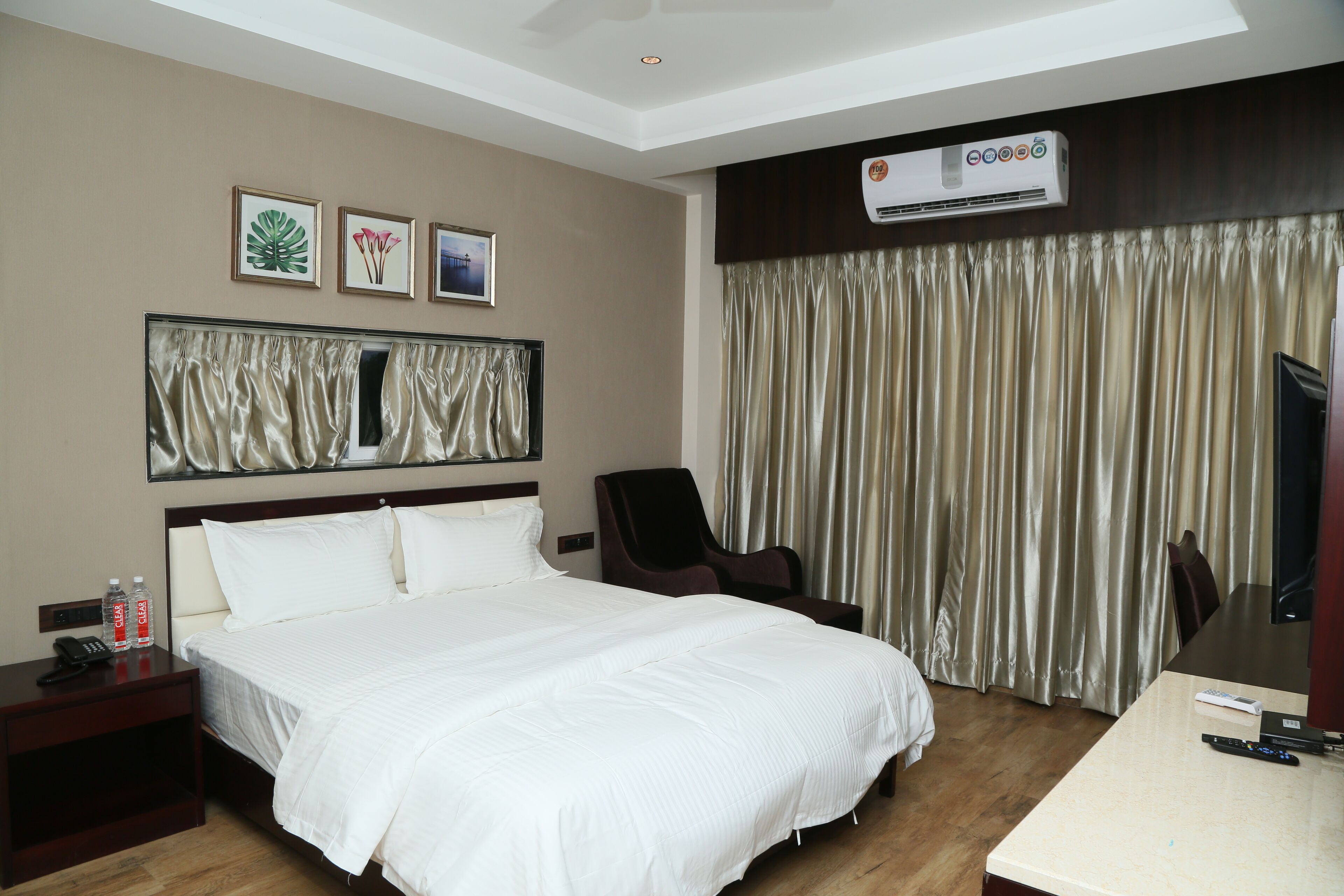 A hotel room with a large bed, a desk, a chair, a TV, and an air conditioning unit.