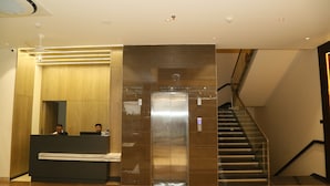 A modern reception area with a reception desk, a large mirror, and a metallic elevator. - Hotel Ruturaj Regency (Dhule)