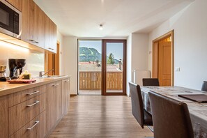 A modern kitchen with wooden cabinets, a built-in microwave, and a large window overlooking a balcony with a mountain view.