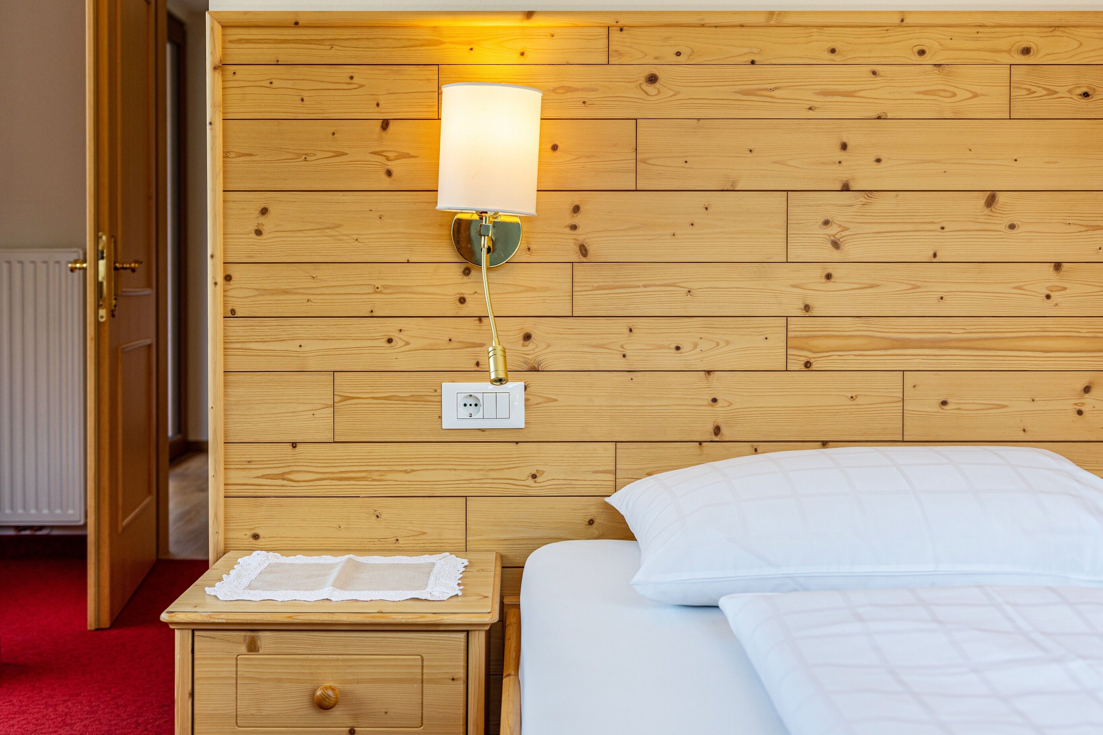 A wooden-paneled room with a bed, a nightstand, a wall-mounted lamp, and a power outlet.