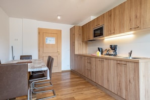 A modern kitchen with wooden cabinets, a built-in microwave, and a dining area with a table and chairs.