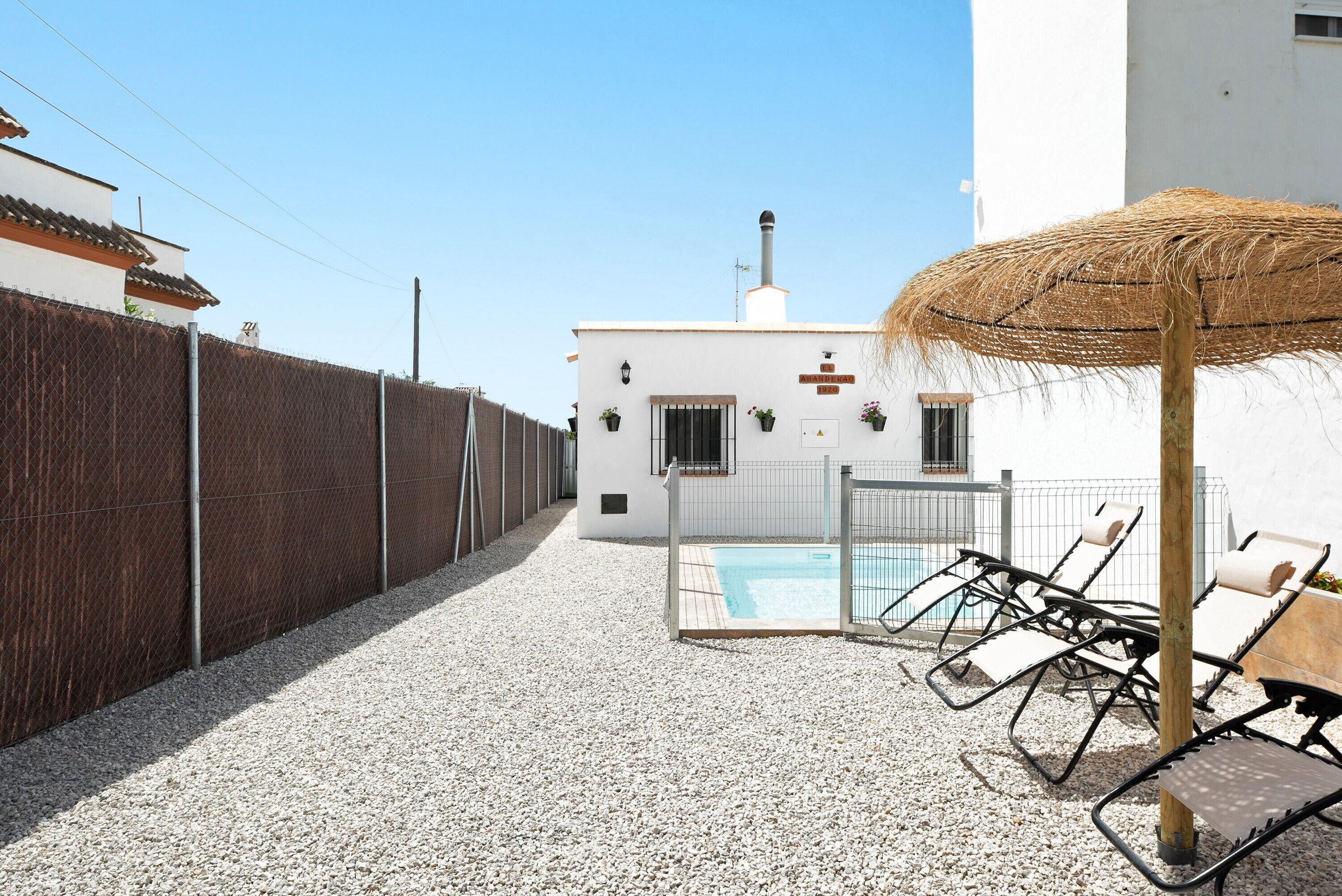 Ein weißes Gebäude mit Pool, Zaun und Liegestühlen.