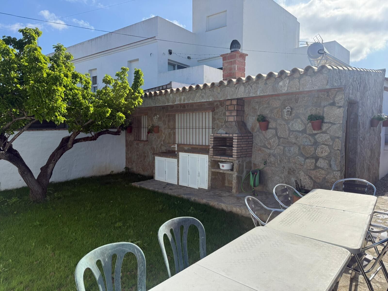 Una cocina al aire libre de piedra con horno de ladrillo, armarios blancos y plantas en macetas.