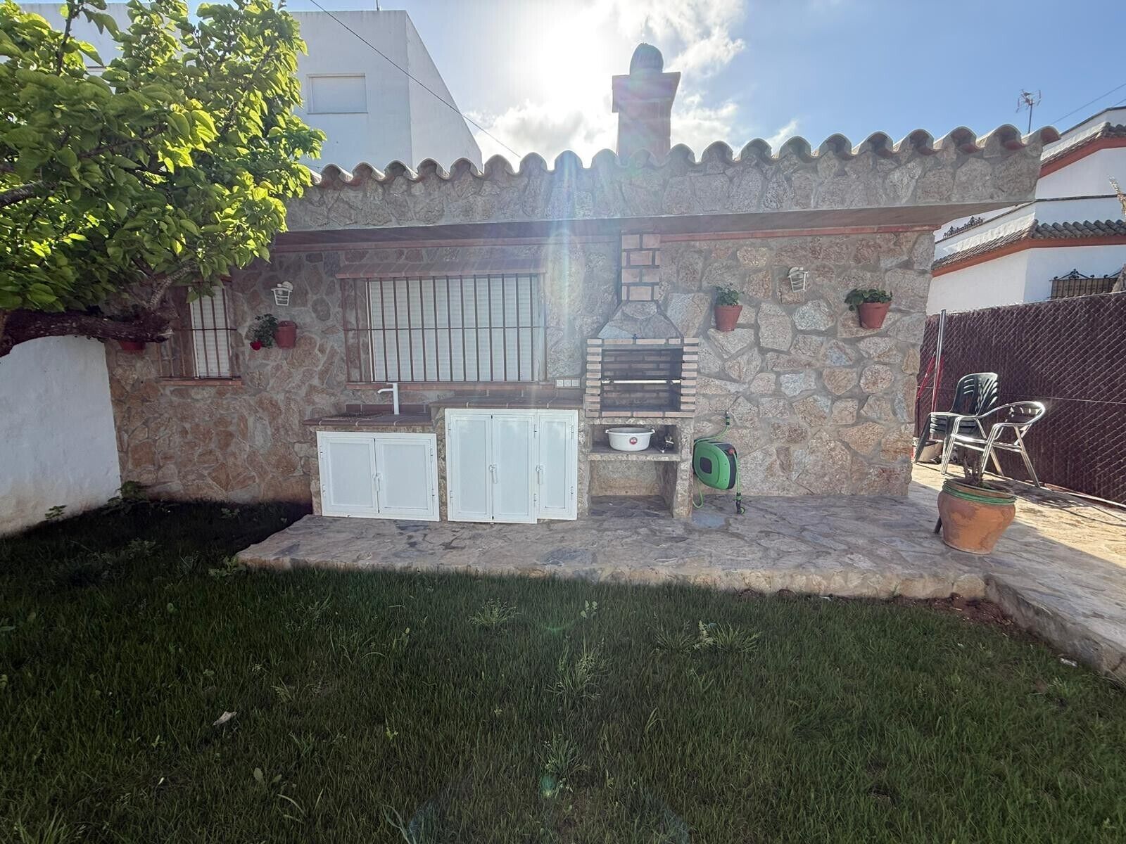 A stone patio with a grill, white cabinets, and potted plants.