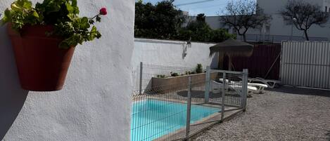 Una piscina rodeada por un área de grava, un muro blanco y una planta en maceta.