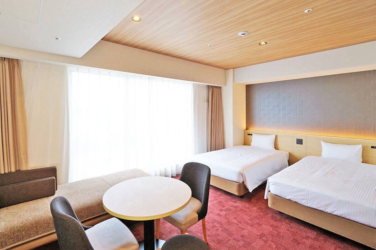 Une chambre d’hôtel avec deux lits, une petite table ronde et un canapé.