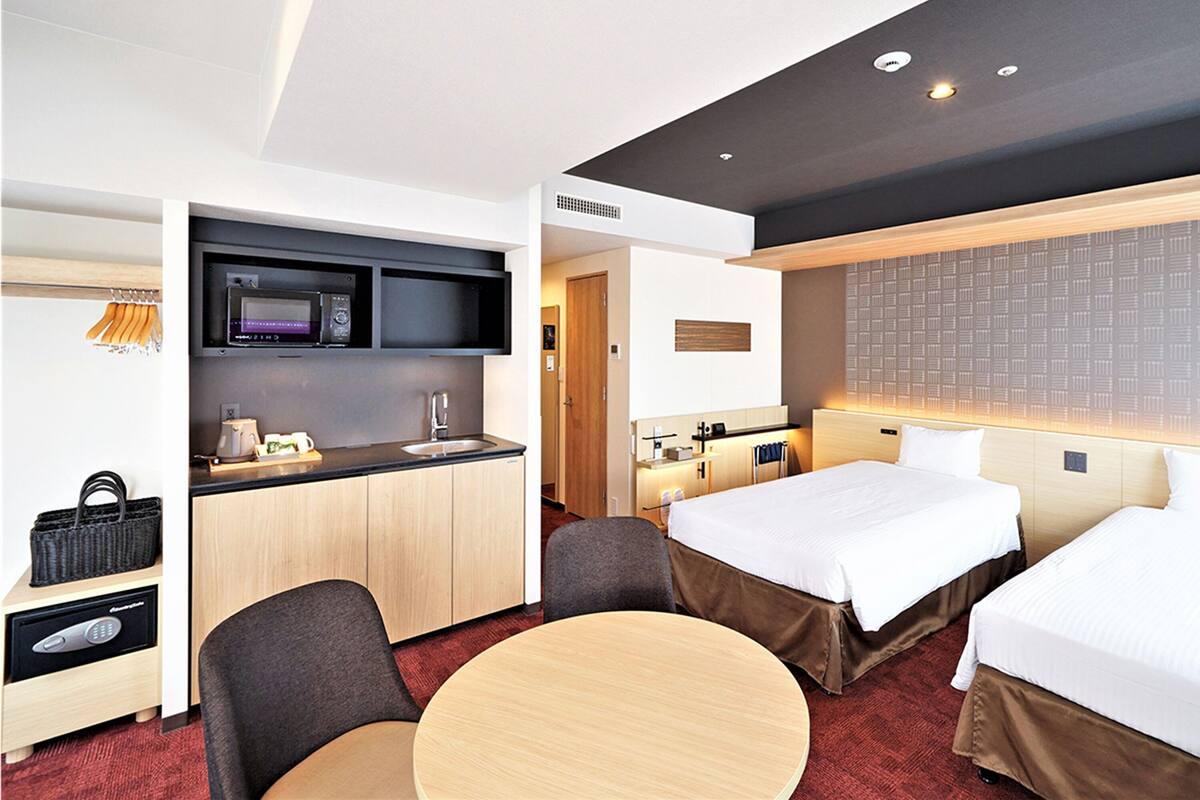 Une chambre d’hôtel équipée d’une kitchenette, de deux lits, d’une table ronde et d’un coin salon.