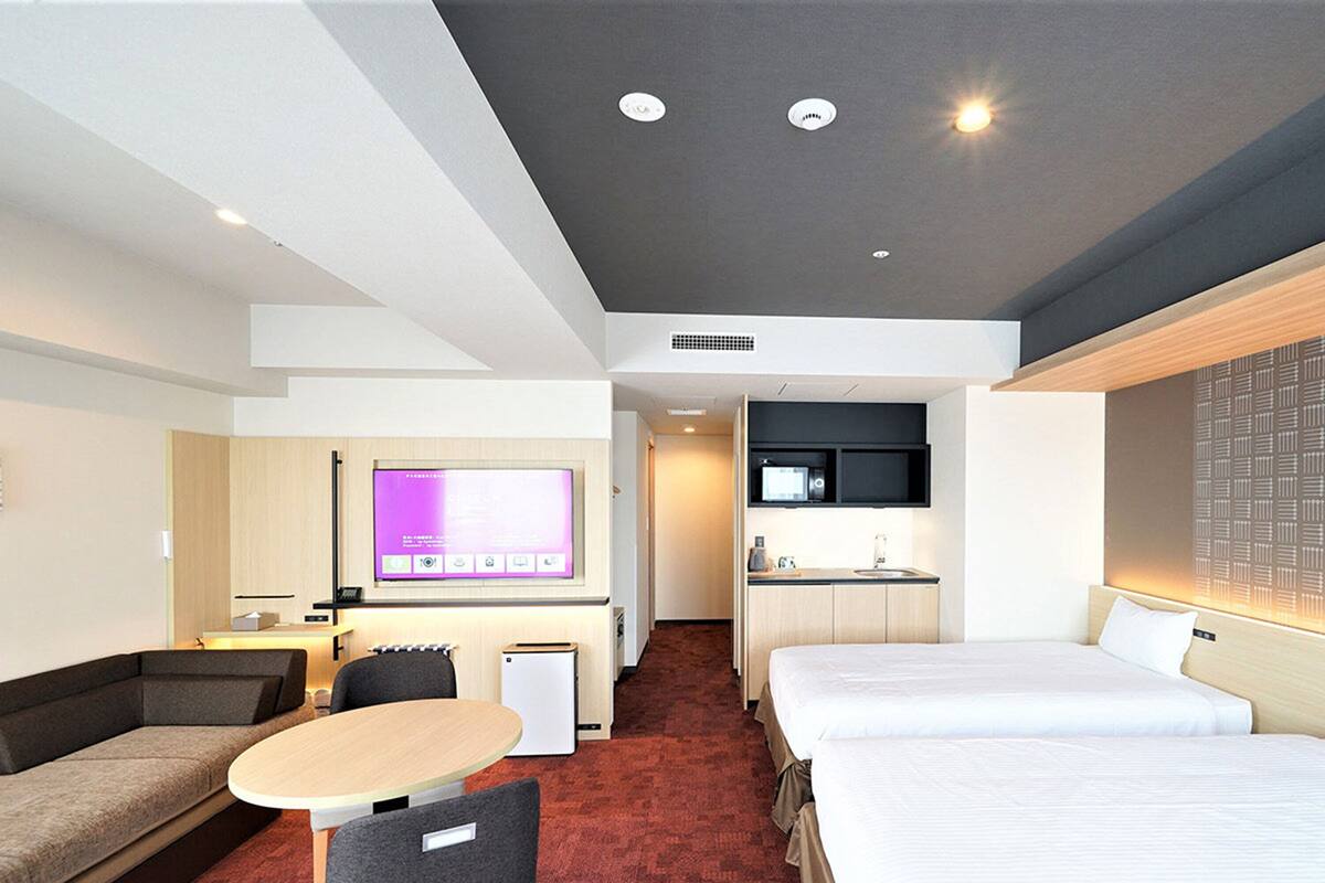 Une chambre d’hôtel équipée d’un lit, d’un canapé, d’un bureau avec un ordinateur, d’une télévision et d’une kitchenette.