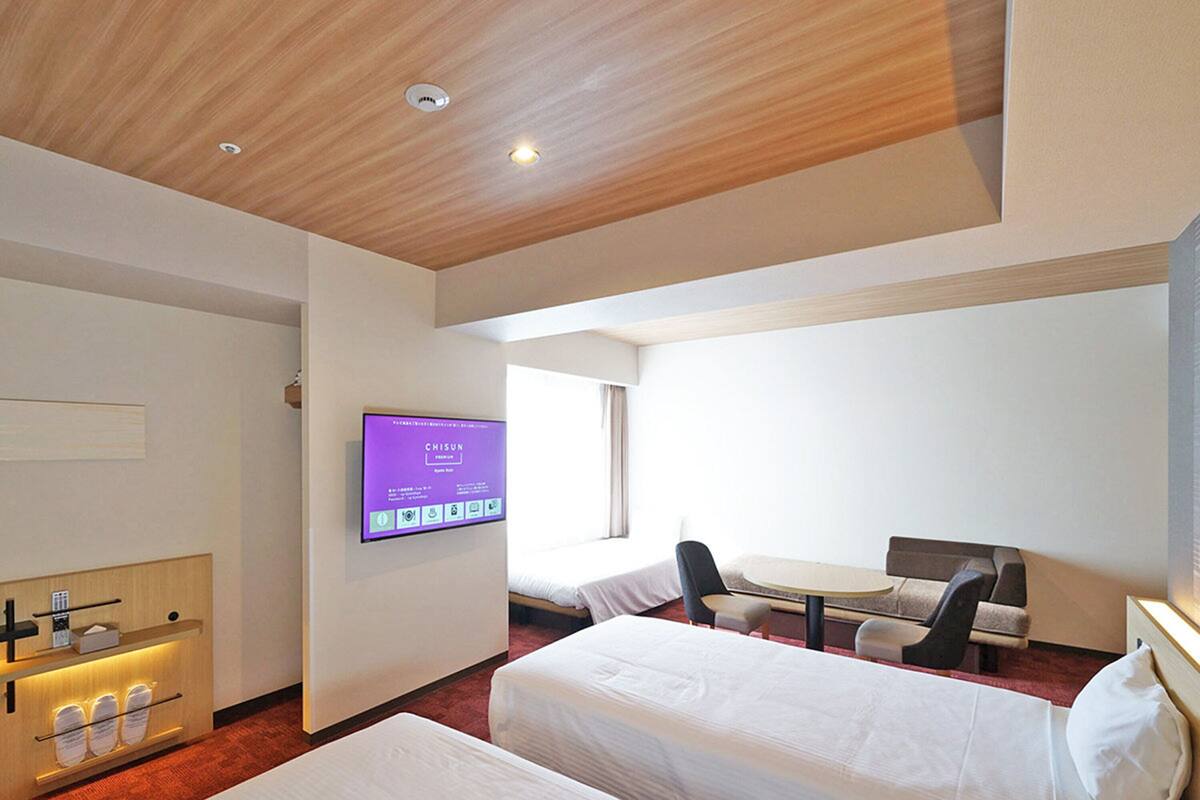 Une chambre d’hôtel avec deux lits, un bureau, une chaise, un téléviseur fixé au mur et un plafond en bois.