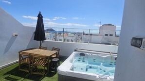 A rooftop terrace with a hot tub, a wooden table, and an umbrella. - Vacation Home Falco 1 close to the Beach with Sea View, Whirlpool & Wi-Fi (Corralejo)