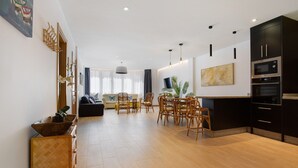 A modern living room with a dining area, kitchen, and a large window. - Vacation Home Falco 1 close to the Beach with Sea View, Whirlpool & Wi-Fi (Corralejo)