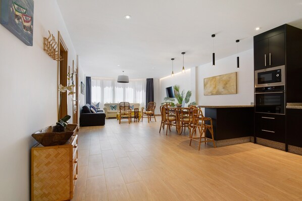 A modern living room with a dining area, kitchen, and a large window.