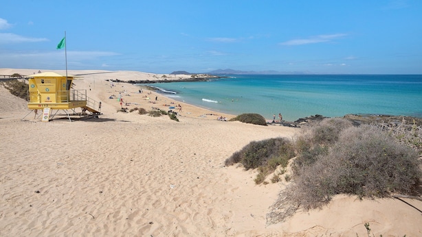 A beach with a lifeguard tower, sandy dunes, and clear blue water. - Vacation Home Falco 1 close to the Beach with Sea View, Whirlpool & Wi-Fi (Corralejo)