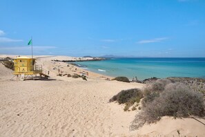 A beach with a lifeguard tower, sandy dunes, and clear blue water.