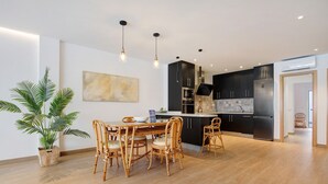A modern kitchen with a dining area, featuring a large potted plant, a dining table with chairs, and a kitchen island with appliances. - Vacation Home Falco 1 close to the Beach with Sea View, Whirlpool & Wi-Fi (Corralejo)