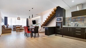 Una cocina moderna con una escalera de madera, un comedor con mesa y sillas, y una sala de estar con sofá y televisor.