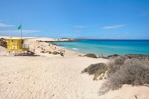 A beach with a lifeguard tower, clear blue water, and sandy dunes.
