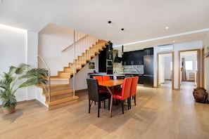 Une cuisine moderne dotée d’un îlot central, d’un coin repas avec une table et des chaises en bois, et d’un escalier menant à un niveau supérieur.
