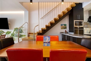 Une cuisine moderne dotée d’un four et d’un micro-ondes encastrés, d’un escalier en bois et d’un coin repas avec une table et des chaises.