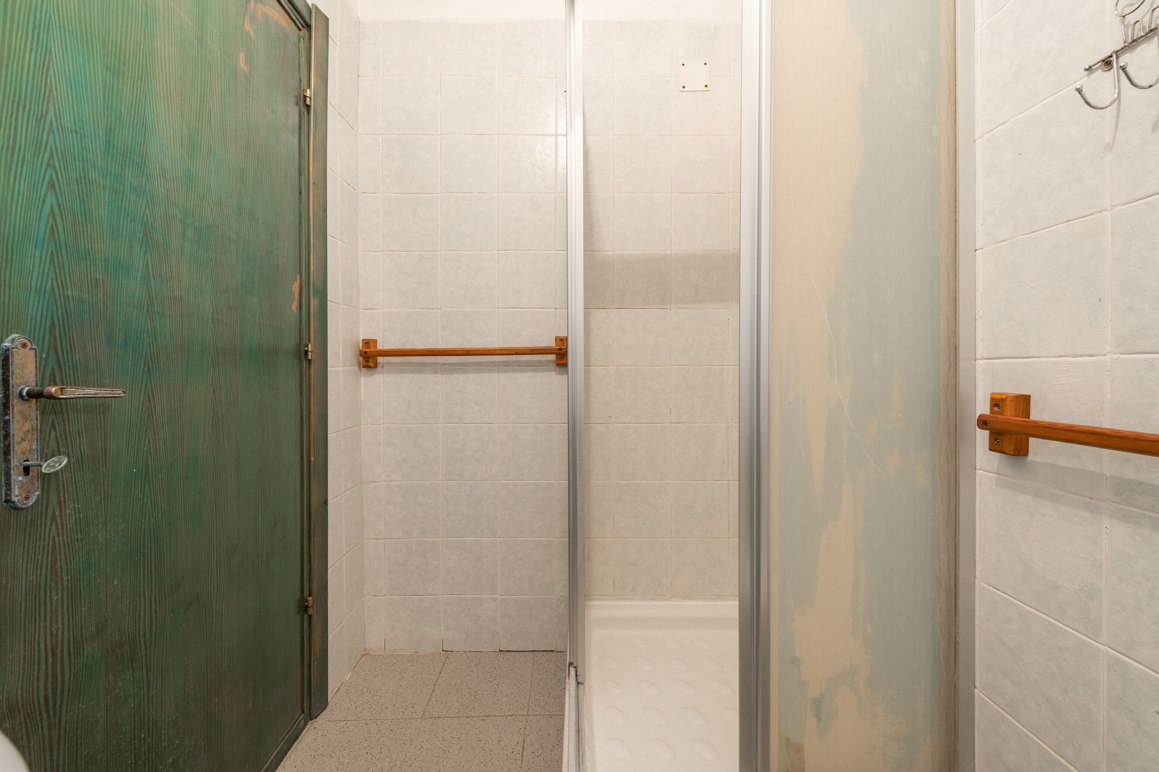 A bathroom with a green door, white tiled walls, a glass shower enclosure, and a wooden towel rack.
