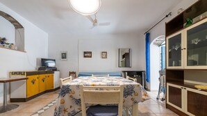 Un comedor con una mesa, sillas, un ventilador de techo, un televisor y una cocina con armarios y un lavamanos.