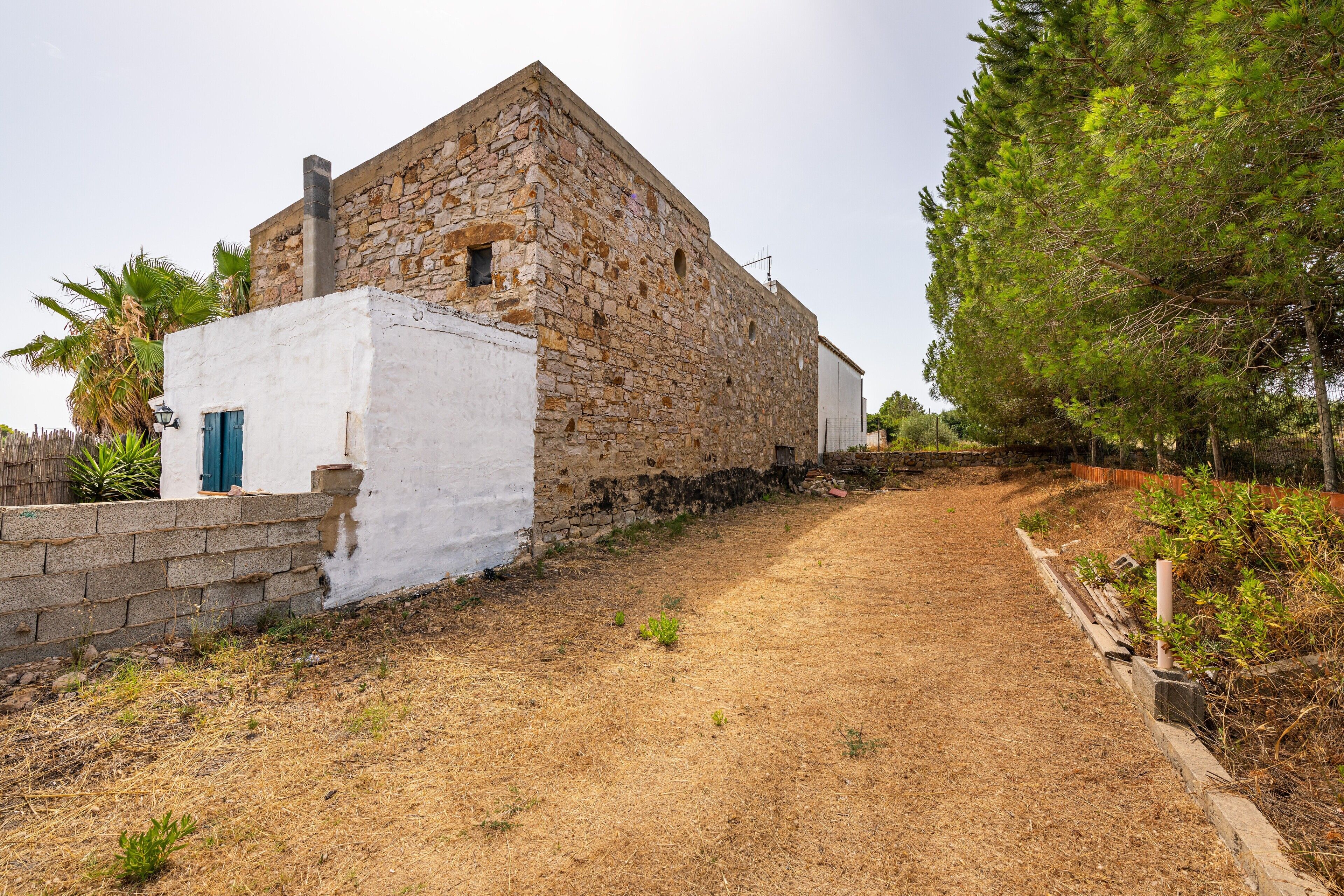Edifici de pedra rústic amb un camí de terra que hi convergeix, envoltat de vegetació.