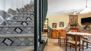 Eine Treppe mit Steinstufen, ein Holzesstisch mit Stühlen, ein Küchenbereich mit einer Steinwand und ein an der Wand befestigtes Fernsehgerät.