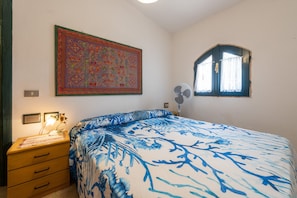 A bedroom with a bed, a dresser, a wall-mounted fan, a window with curtains, and a large decorative painting.