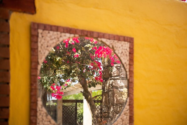 A circular mirror reflecting a tree with pink flowers, set against a yellow wall with a brick pattern.