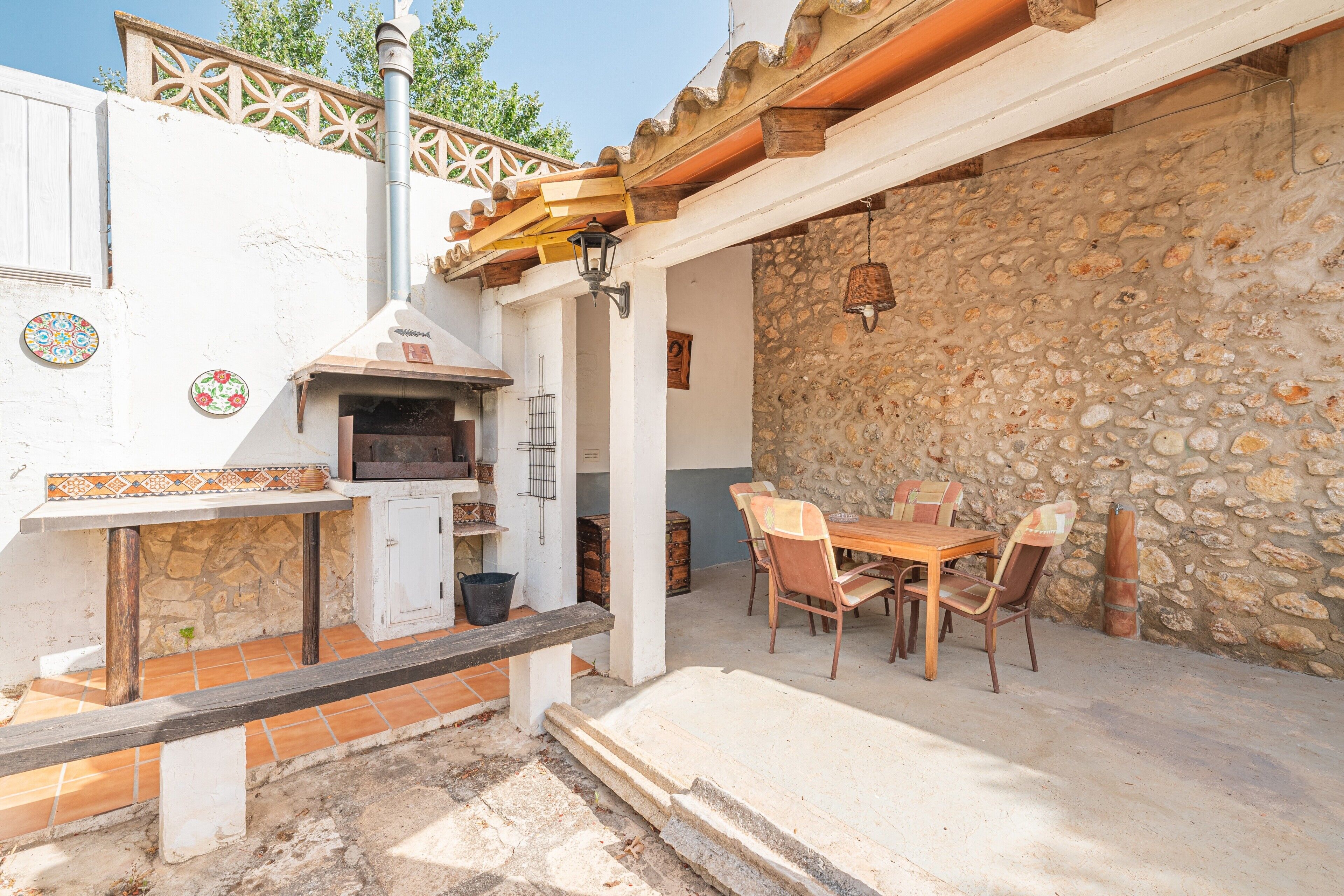 An outdoor patio with a stone wall, a wooden table with chairs, and a pizza oven.