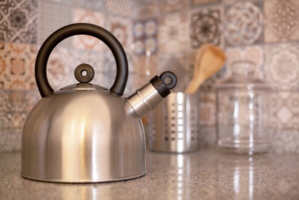 A stainless steel kettle with a black handle on a kitchen counter.