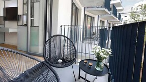 Un balcón con una silla negra, una mesa pequeña con un florero y una puerta de vidrio que da a un edificio moderno.